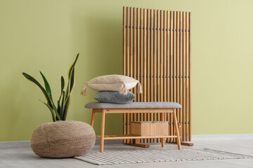 Beautiful interior of living room with cozy bench, houseplant, pillows and folding screen