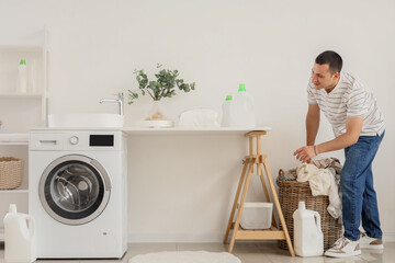 Young man taking dirty clothes from basket in laundry room