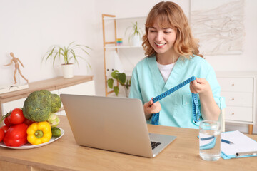 Female nutritionist with tape measure video chatting at table in kitchen