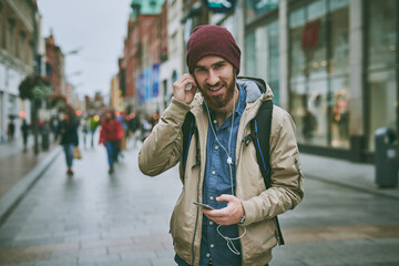 Travel, city and portrait of man with phone for music, streaming subscription and walking in street. Urban town, happy and person on smartphone with earphones for listening to radio, audio or podcast