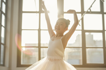 Young ballerina in a white tutu practicing in a sunlit studio. Bright, cheerful expression highlighting her joy and dedication to dance