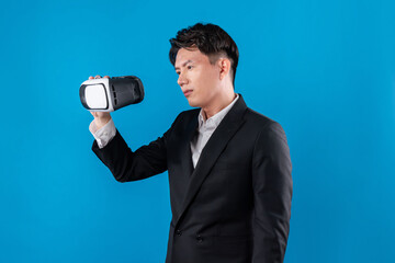 Asian businessman in serious face checking through VR connecting to financial report in futuristic metaverse data analytics communication technology virtual reality at blue copyspace. Contrivance.