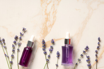 Bottles of lavender essential oil and flowers on marble background