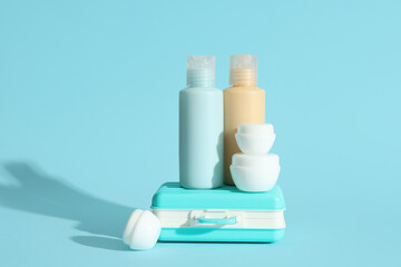 Travel cosmetic kit and mini suitcase on color background