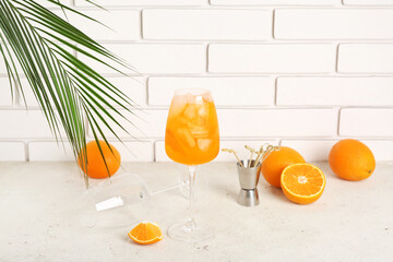 Glass of Aperol spritz cocktail with palm leaf and oranges on white table