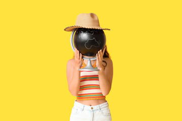 Young Asian woman hiding her face behind globe on yellow background. Travel concept