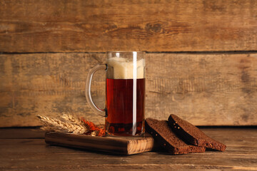 Mug of fresh kvass with slices of bread and wheat on wooden background