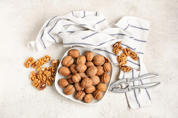 Plate with tasty walnuts and nutcracker on white background