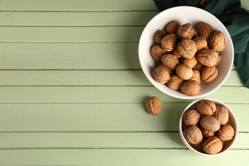 Bowls with tasty walnuts on green wooden background