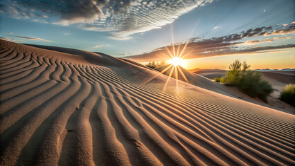 Naklejka premium A wide shot of the sun setting behind a sweeping desert dune, casting long shadows