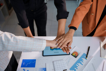 Business team joining hands showing teamwork and support over a desk with charts and graphs, symbolizing unity and collaboration
