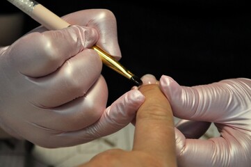 Manicurist with a brush apply gel polish.Female master in the salon is painting with brush on the hands of the client. 