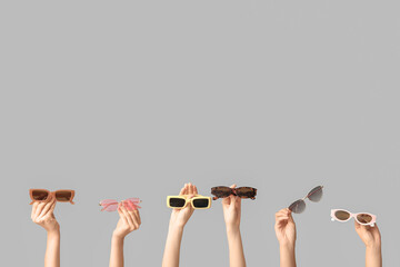 Female hands with many stylish sunglasses on grey background