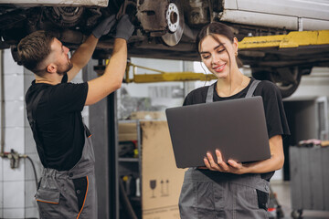 Young expert female inspects repair checklist with automotive mechanic worker partner, quality suspension technician team at fix garage. Vehicle maintenance service works industry occupation job.
