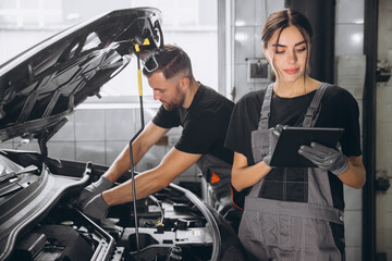 Auto service, repair, maintenance concept. Mechanic checks the car at the service station. Charming woman and bearded engineer use tablet check car battery