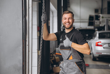 Happy bearded male mechanic in gray uniform opens service station door and shows thumb up