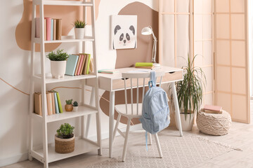 Modern school desk with stationery and backpack in room near color wall