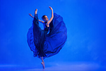 young ballerina in pointe shoes dances in a blue dress with a flying skirt