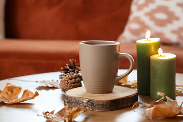 Cup of tea with burning candles and autumn leaves on table in living room, closeup