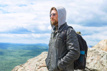A man in a gray jacket stands on a mountain peak in a hood.
