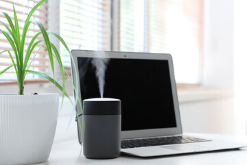 Air humidifier with plant and laptop on table in office, closeup