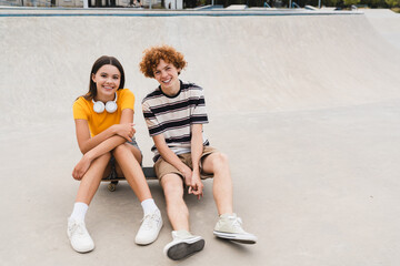 Carefree boy girl skaters friends teenagers sitting on skateboard have fun on urban street at summer spending time holiday together in skate park ramp after school lessons looking at camera copy space
