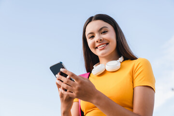 Smiling hispanic teen school girl teenager student pupil in casual clothing holds smart cell phone...