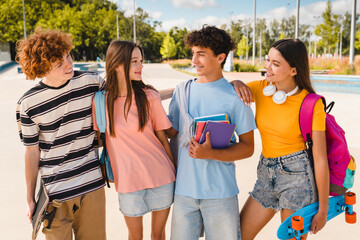 Group of smiling diversity teenagers high school pupils friends classmates college students boys and girls with bags skateboards meeting talking communicating hanging out in skate park outside