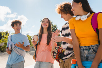 Multiethnic friends students guys girls teenagers school pupils hanging outside on a sunny day having fun walking on city street urban nature park enjoying summer vacation together. Friendship concept