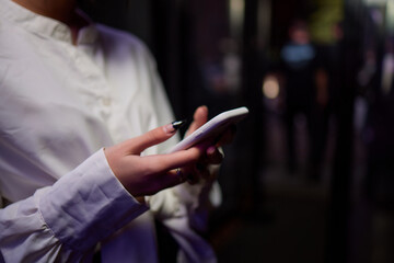 Woman in stylish dress with chic manicure using smartphone in closeup shot in nightclub