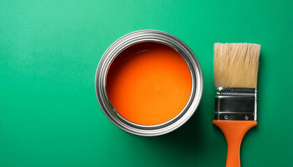 Metal can with orange paint and brush. Flat lay on green backdrop. Close-up.