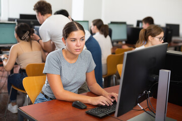 Fototapeta premium Woman sitting at desk in computer class and using PC, learning to use software.