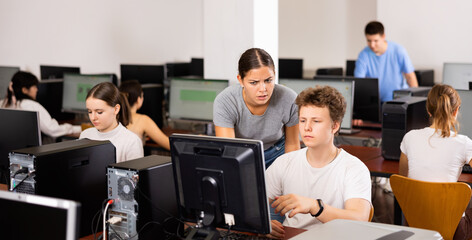 Fototapeta premium Schoolboy using computer and teacher helping to him in classroom
