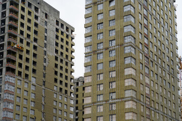 Workers continue construction on tall residential buildings with scaffoldings, amidst cloudy skies in an urban setting