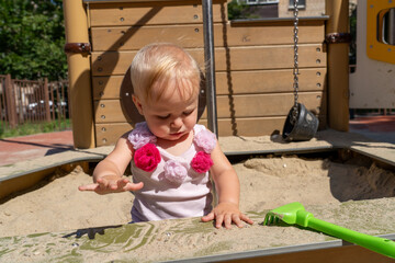 A young child is happily digging in the sand at a playground, enjoying the tactile experience with brightly colored toys