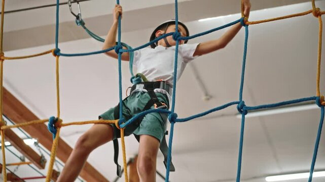 The camera zooms in on a boy who is in a hurry to pass an obstacle course in a rope pair consisting of a rope web. The athletic boy shows his tenacity and dexterity. High quality 4k footage
