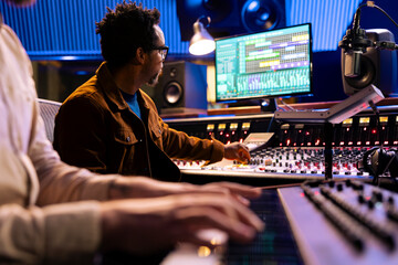 African american audio expert records artist playing piano in studio, using mixing console and...