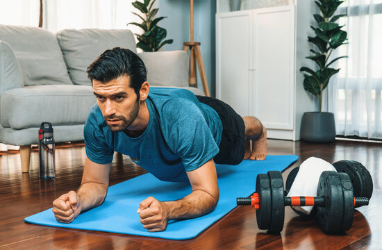 Athletic and sporty man doing plank on fitness mat during home body workout exercise session for fit physique and healthy sport lifestyle at home. Gaiety home exercise workout training.
