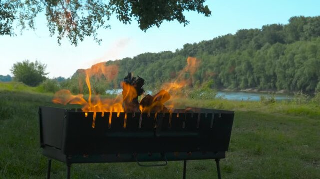 Field time with fire for bbq outdoor. A view of field place with metal box with burning woods before cooking in summer.