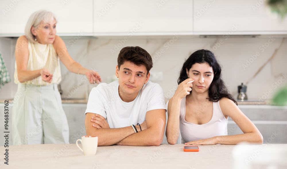 Wall mural portrait of an offended married couple in a home kitchen, which mature mother reprimand. family conf