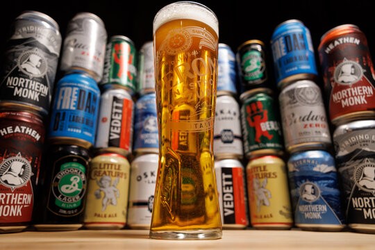 Pint of Peroni Beer in Front of a Wall of Various Beer Cans: Featuring Lagers, IPAs, and Ales in a Colorful Display
