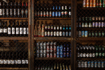 A row of beer bottles and cans are on a shelf. The bottles are of various sizes and colors, and the cans are also of different sizes and colors. The shelf is filled with a variety of beer