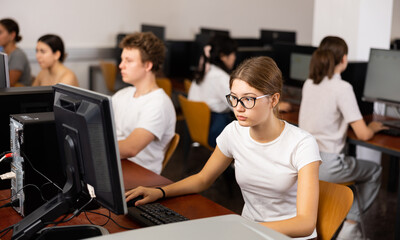 Fototapeta premium Teenage girl in glasses sitting at table and using computer during lesson.