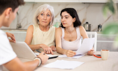 Young male realtor is discussing the terms of real estate sale with an elderly woman and her adult daughter