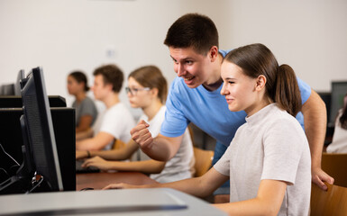 Fototapeta premium Positive male student explaining the topic to female friend while she is studying computer science on the pc in the classroom