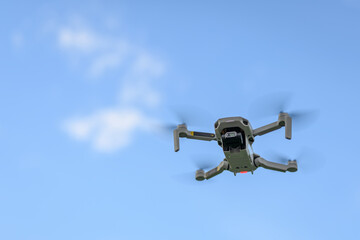 A small drone flying with a blue sky in the background.