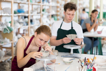 Teenage boy and teenage girl students in apron make clay product in ceramic workshop