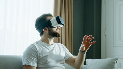 A man in a white t-shirt wearing a VR headset is fully immersed in a virtual reality experience, extending his hand as he interacts with the digital environment. 