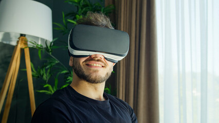 Smiling man immersed in a virtual reality experience wears a VR headset, interact with the digital...