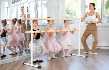 Little girls doing ballet at group training session in the studio performs demi plie near the ballet barre, standing in a ballet stance © JackF